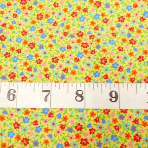 May include: A yellow fabric with a small floral print in red, orange, blue, and pink. A white measuring tape with black numbers is placed on top of the fabric. The numbers on the tape read 5, 6, 7, 8, 9, and 10.