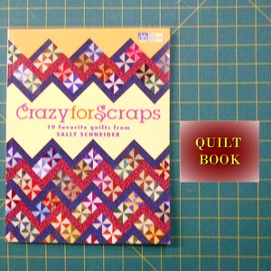 May include: A yellow book with the title "Crazy for Scraps" and the subtitle "19 favorite quilts from Sally Schneider". The book cover features a colorful quilt pattern with red, blue, and yellow fabric. The book is on a green cutting mat with a red label that says "QUILT BOOK".