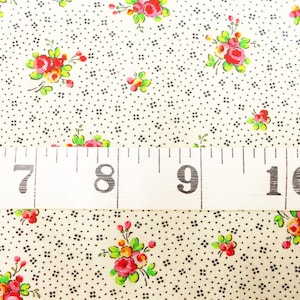May include: A white fabric with a repeating pattern of small black diamonds and larger red, pink, and yellow floral bouquets. A white measuring tape with black markings shows the numbers 7, 8, 9, and 10.