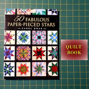 May include: A book titled "50 Fabulous Paper-Pieced Stars" by Carol Doak. The cover features a collage of colorful star quilt blocks. The book is labeled "Quilt Book".