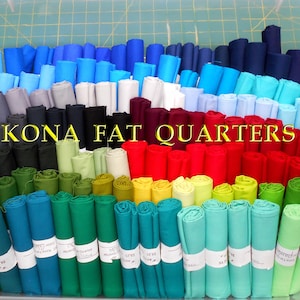 May include: A large collection of rolled fabric pieces known as Kona Fat Quarters, arranged in a clear plastic bin. The fabric rolls display a wide spectrum of colors including blues, purples, whites, blacks, reds, yellows, and greens.