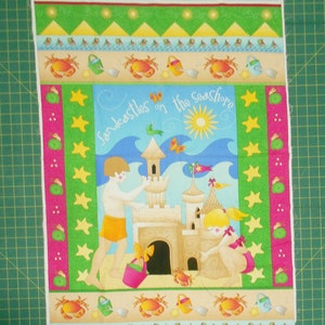 May include: A colorful fabric panel with a beach theme. It features a sandcastle with two children building it, a yellow sun, blue waves, and green palm trees. The text "Sandcastles on the Seashore" is written in a whimsical font. The panel is bordered with a repeating pattern of stars, seashells, and crabs.