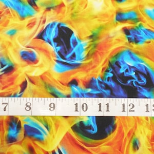 May include: Abstract fabric with a swirling pattern of blue, yellow, orange, and green flames. The fabric is measured with a white tape measure.