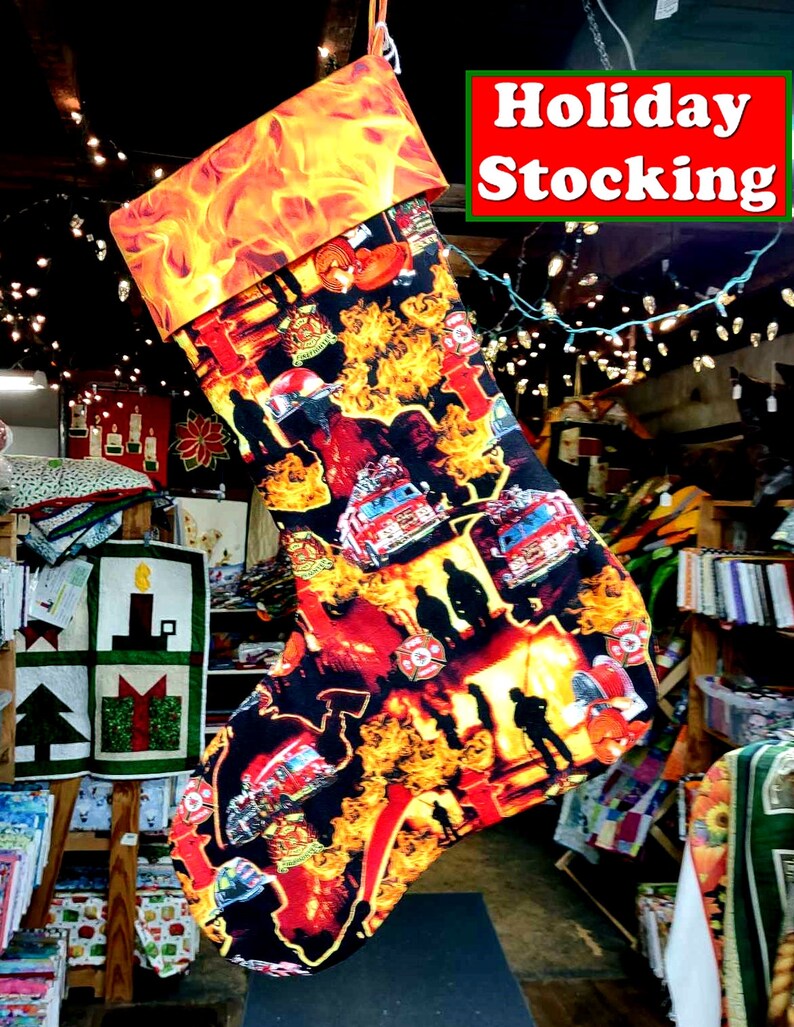 May include: A red and black Christmas stocking with a fire engine and firefighter theme. The stocking has a bright orange cuff with flames printed on it. The text "Holiday Stocking" is printed in white on a green background.