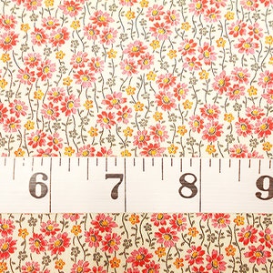 May include: A close-up of a white fabric with a repeating pattern of small pink and yellow flowers. A white measuring tape with black markings is placed across the fabric, showing the numbers 5, 6, 7, 8, and 9 inches.