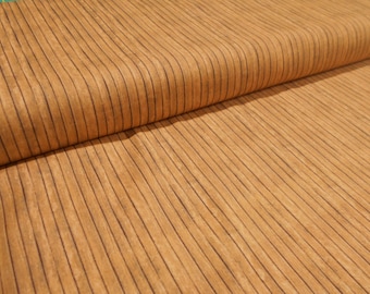 May include: Close-up of a tan fabric with vertical, dark brown lines. The fabric is folded over, revealing the texture and pattern. The material has a warm, natural color and a subtle sheen, suggesting a soft, pliable texture.