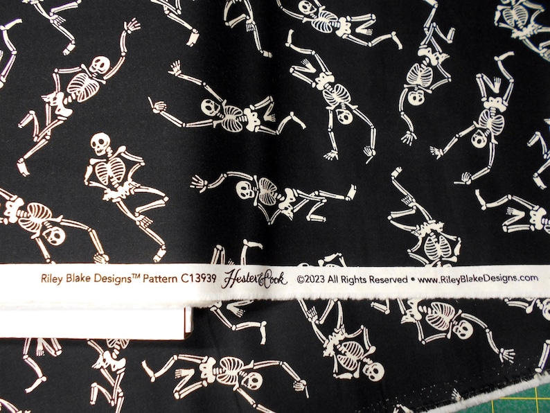 Peut inclure: Tissu noir avec un motif blanc r&eacute;p&eacute;t&eacute; de squelettes dansant. Le tissu a une &eacute;tiquette blanche qui indique "Riley Blake Designs&trade; Pattern C13939 Hester & Cook &copy;2023 All Rights Reserved - www.RileyBlakeDesigns.com"