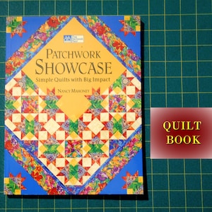 May include: A book titled "Patchwork Showcase: Simple Quilts with Big Impact" by Nancy Mahoney. The cover features a colorful patchwork quilt design with a red, yellow, blue, and green color scheme. The book is labeled "Quilt Book" in a red box.