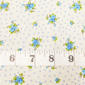 May include: A close-up of a white fabric with a repeating pattern of small blue flowers. A white measuring tape with black markings is placed across the fabric, showing measurements from 5 to 10 inches.