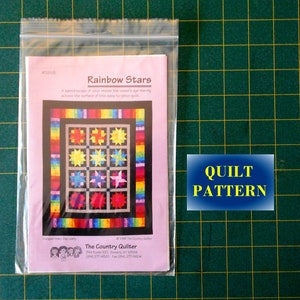 May include: A pink and white quilt pattern with a rainbow border and a black background. The pattern features a variety of colorful stars. The pattern is titled "Rainbow Stars" and is from "The Country Quilter".