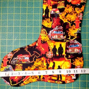 May include: Firefighter themed Christmas stocking with a red fire truck, fire hydrant, and flames. The stocking is 12 inches long.
