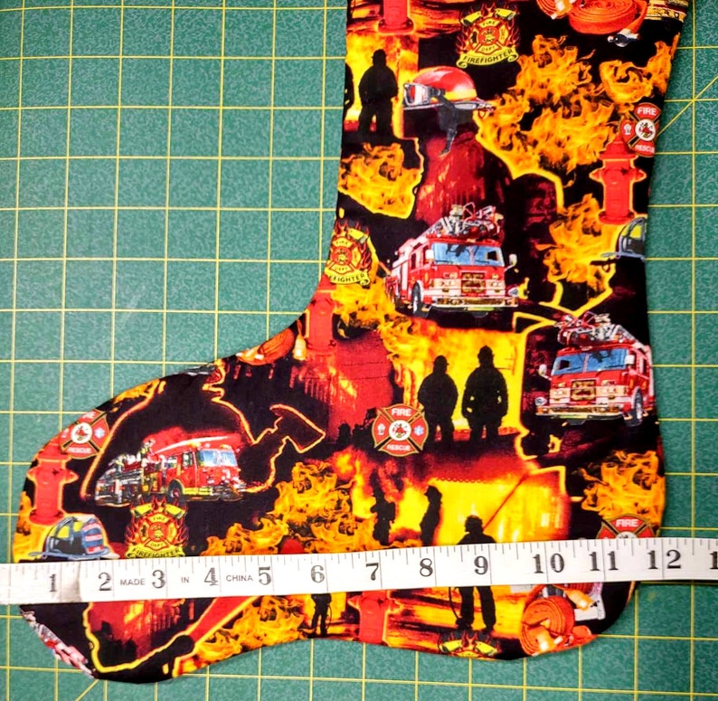 May include: Firefighter themed Christmas stocking with a red fire truck, fire hydrant, and flames. The stocking is 12 inches long.