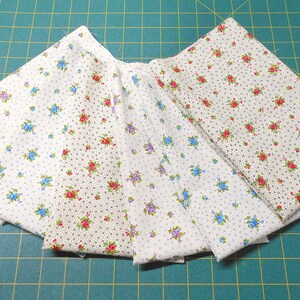 May include: Five fabric swatches with a white background and a small floral pattern. The patterns include red, blue, and purple flowers.