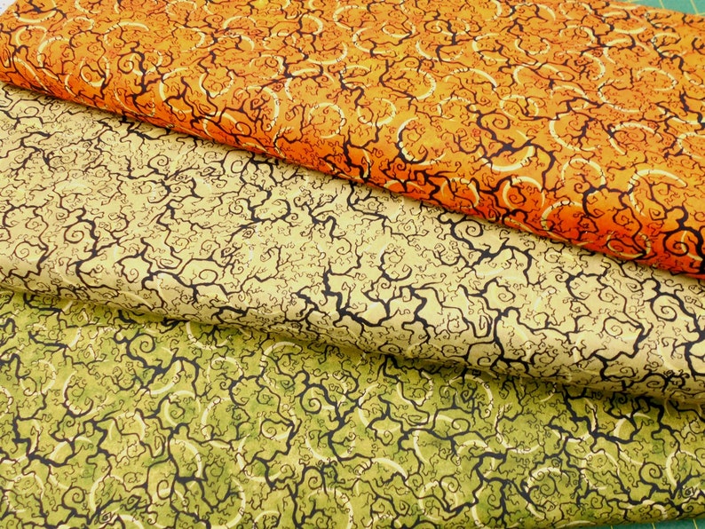 May include: Three fabric swatches with a swirling, vine-like pattern. The top swatch is orange, the middle swatch is beige, and the bottom swatch is green.