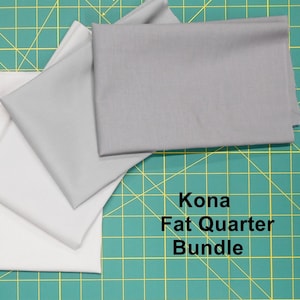 May include: A bundle of Kona fat quarters in shades of gray and white, neatly folded. The fabric is arranged on a green cutting mat. Text on the image reads "Kona Fat Quarter Bundle."