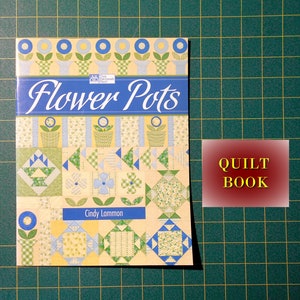 May include: A book titled "Flower Pots" by Cindy Lammon. The cover features a colorful patchwork quilt design with flowers, pots, and geometric shapes. The book is a quilting pattern book.
