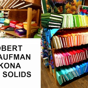 May include: A shelf display of Robert Kaufman Kona Solids fabric in a variety of colors. The fabric is arranged in rows by color, starting with green and ending with blue.