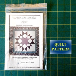 May include: A white paper pattern for a quilt called "Green Mountain Star" designed by Ramona Sturtevant. The pattern includes instructions for a 80-inch square quilt, as well as two sizes of table runners and placemats.