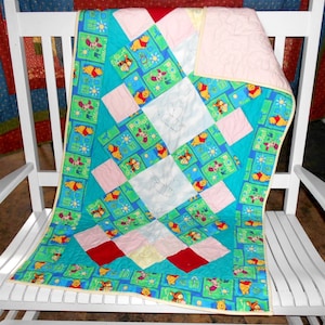 May include: A Winnie the Pooh baby quilt with a blue, green, pink, and red patchwork design. The quilt features a variety of Winnie the Pooh characters and the text "Pooh-Bah" in a yellow sun.