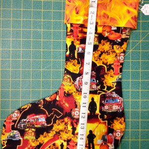 May include: A red and yellow Christmas stocking with a fire truck and firefighter theme. The stocking is 17 inches long and has a cuff with flames.