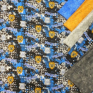 May include: Black fabric with a blue and white splatter pattern and repeated text "Police". The fabric is layered with other fabrics in orange, gray, and blue.
