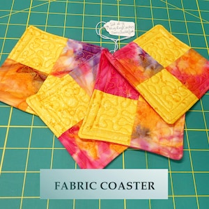 May include: Set of four fabric coasters with a yellow and orange tie-dye pattern. The coasters are quilted and have a decorative stitch around the edges. The text "Set of 4 Fabric Coasters" is visible on a tag.