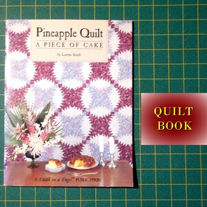 May include: A book titled "Pineapple Quilt: A Piece of Cake" by Letta Smith. The cover features a quilt pattern with pink and blue colors. The book is a "Quilt in a Day" publication.