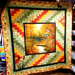 May include: A large, handmade quilt with a central landscape scene of a pond surrounded by autumn trees. The quilt features a colorful patchwork border in shades of red, yellow, green, and gray, with a floral patterned edge.