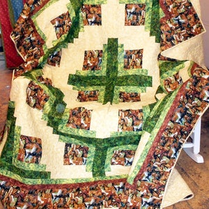 May include: A quilt with a green and brown patchwork design featuring a pattern of horses. The quilt is made with a cream-colored fabric and has a brown and green border.