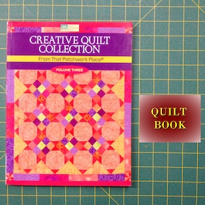 May include: A book titled "Creative Quilt Collection" from "That Patchwork Place" Volume Three. The cover features a quilt with a star pattern in shades of pink, orange, yellow, and purple. The text "QUILT BOOK" is on a red background.