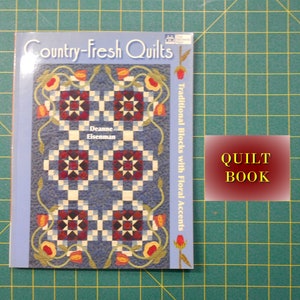 May include: A book titled "Country-Fresh Quilts: Traditional Blocks with Floral Accents" by Deanne Eisenman. The cover features a quilt design with red, white, and blue squares and floral accents.