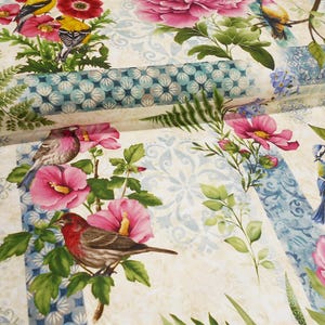 May include: A white fabric with a floral pattern featuring pink and white flowers, blue birds, and yellow birds. The fabric has a blue and white geometric pattern in the background.
