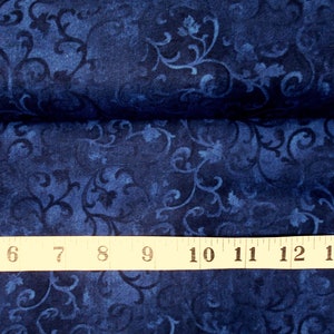 May include: A close-up of a dark blue fabric with a white floral pattern. A measuring tape is placed on top of the fabric, showing measurements from 5 to 14 inches.