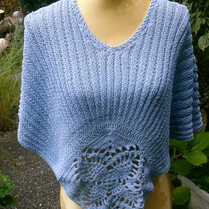 Könnte beinhalten: Ein hellblaues gestricktes Poncho mit einem gehäkelten Design am unteren Rand.
