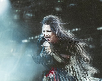 May include: A woman with long dark hair sings into a microphone while performing on stage. She is wearing a black and white outfit with a long flowing skirt.