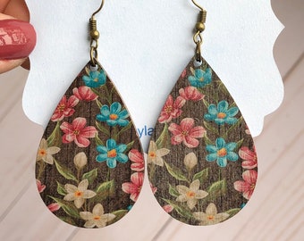 May include: A pair of wooden teardrop-shaped earrings with a floral print. The earrings are brown with pink, white, and blue flowers. The earrings have gold hooks.