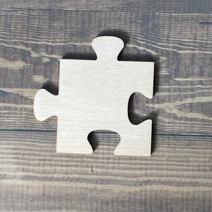 Peut inclure: Une pi&egrave;ce de puzzle en bois en forme de pi&egrave;ce de puzzle. La pi&egrave;ce est de couleur brun clair et a une surface lisse.