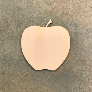 May include: A wooden apple-shaped cutout with a stem. The cutout is made of light-colored wood and has a smooth surface. The apple shape is a simple, clean design, perfect for crafts or decorations.