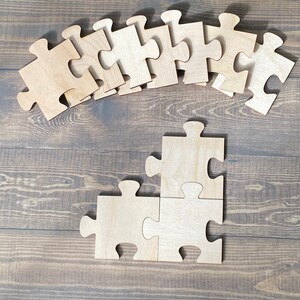 Peut inclure: Un ensemble de pi&egrave;ces de puzzle en bois en forme de puzzle. Les pi&egrave;ces sont dispos&eacute;es en ligne courbe en haut de l'image, et deux pi&egrave;ces sont assembl&eacute;es en bas de l'image.