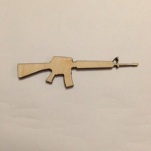 May include: A wooden silhouette of a rifle, cut out from a light brown piece of wood.