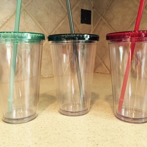 May include: Three clear plastic tumblers with lids and straws. The lids are green, red, and green. The straws are green, gray, and red.