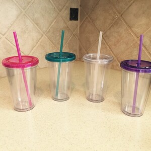 May include: Four clear plastic tumblers with lids and straws. The lids are pink, teal, clear, and purple. The straws are pink, teal, clear, and purple.