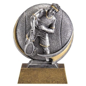 May include: Silver tennis trophy with a sculpted figure of a player holding a racket. The trophy has a round base with a textured surface and a gold-colored trim.