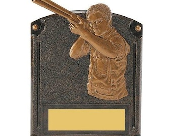 May include: A bronze-colored award plaque with a sculpted image of a person shooting a shotgun. The plaque has a rectangular gold-colored plate for engraving.