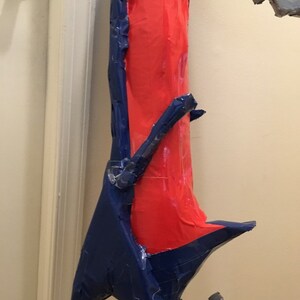 May include: A red and blue cardboard prop, possibly a weapon or a part of a costume. The prop is made of cardboard and covered in blue and red tape.