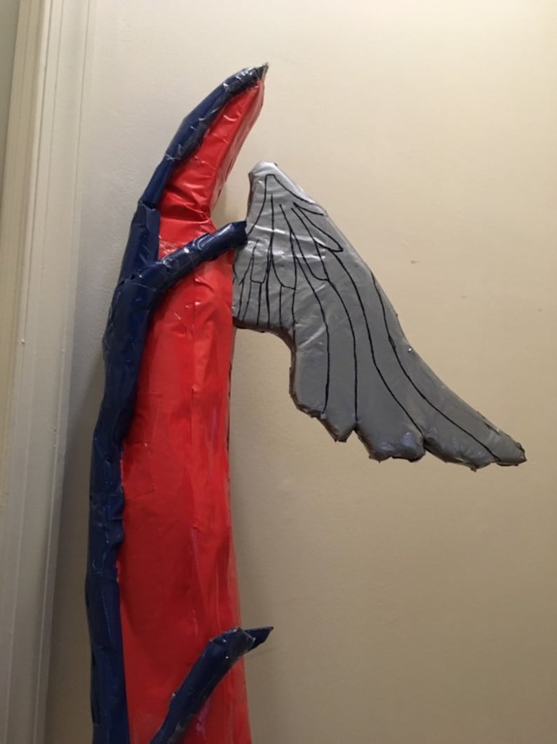 May include: A red and blue cardboard sculpture of an angel with a single wing. The wing is made of gray cardboard and has a detailed design.