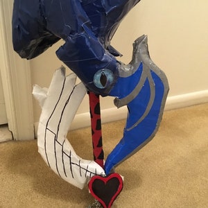 May include: A blue and silver cardboard keyblade with a red and black handle and a black heart charm with a chain.