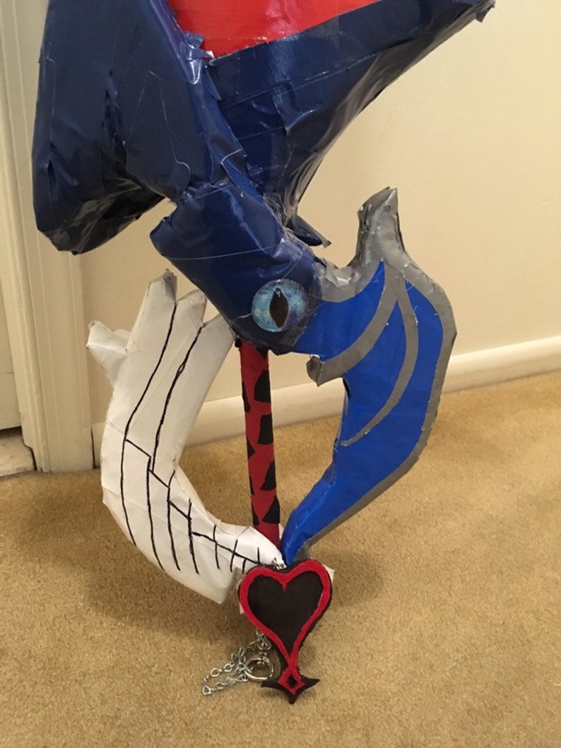 May include: A blue and silver cardboard keyblade with a red and black handle and a black heart charm with a chain.