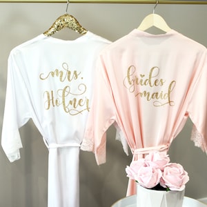 May include: Two satin robes with lace trim, one white with "mrs. Hofner" in gold glitter lettering and one pink with "bridesmaid" in gold glitter lettering.