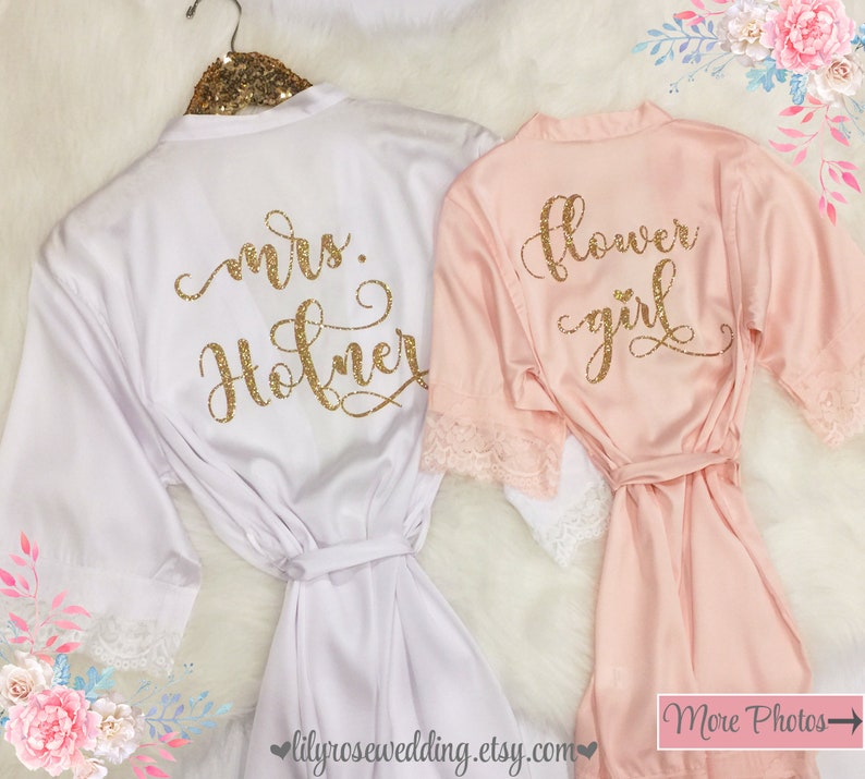 May include: Two satin robes with lace trim. The white robe has "mrs. Holner" written on the back in gold glitter. The pink robe has "flower girl" written on the back in gold glitter.